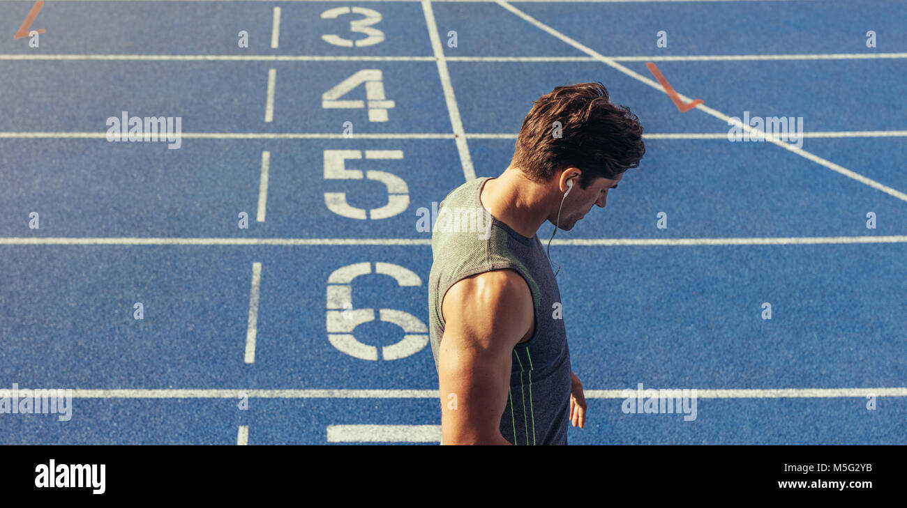 Athlete standing on a running track near the start line. Runner wearing earphones standing on the running track. Stock Photo