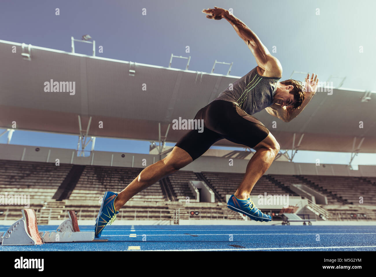 Athlete starting his sprint on an all-weather running track. Runner using starting block to start his run on running track in a stadium. Stock Photo