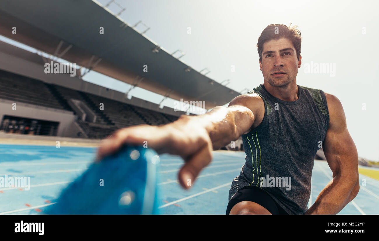 Athlete doing stretching exercises on running track. Runner stretching leg muscles by touching his shoes. Stock Photo