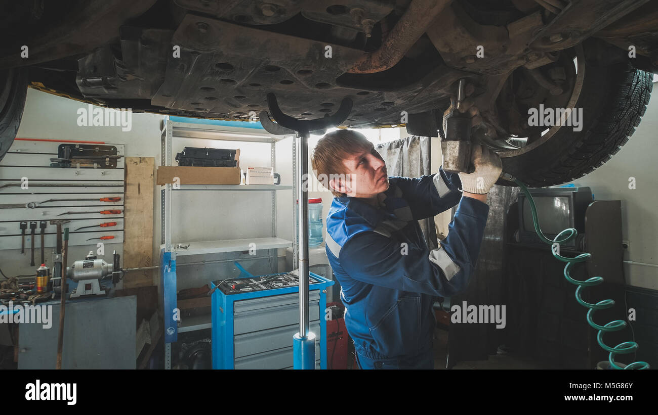 Mechanic unscrewing parts of automobile's bottom under lifted car Stock Photo