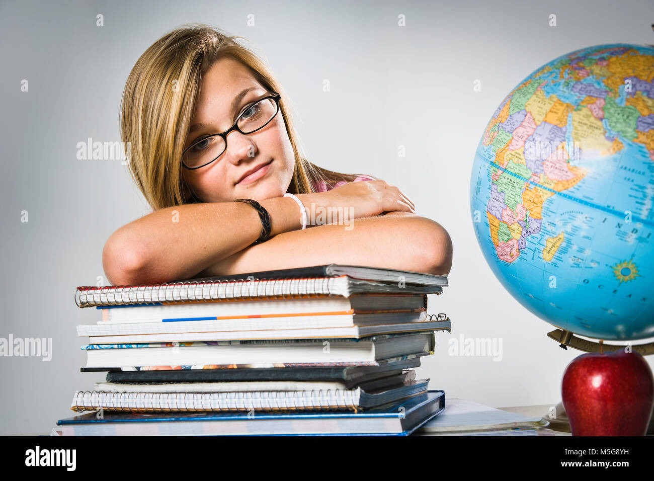 Teenage girl with glasses leaning on stack of books Stock Photo