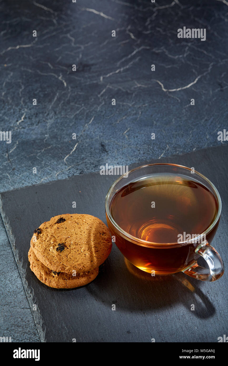 A transparent glass cup of black tea with chocolate chips cookies on a ...