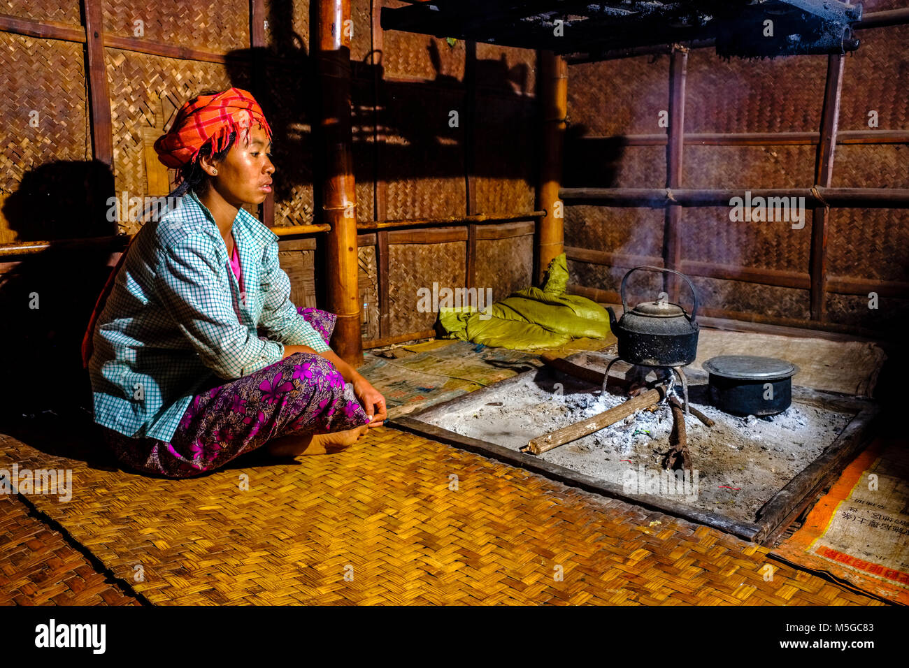 A farmers woman is sitting at the fire place in her bamboo house in a village in the hills of the tribal area Stock Photo