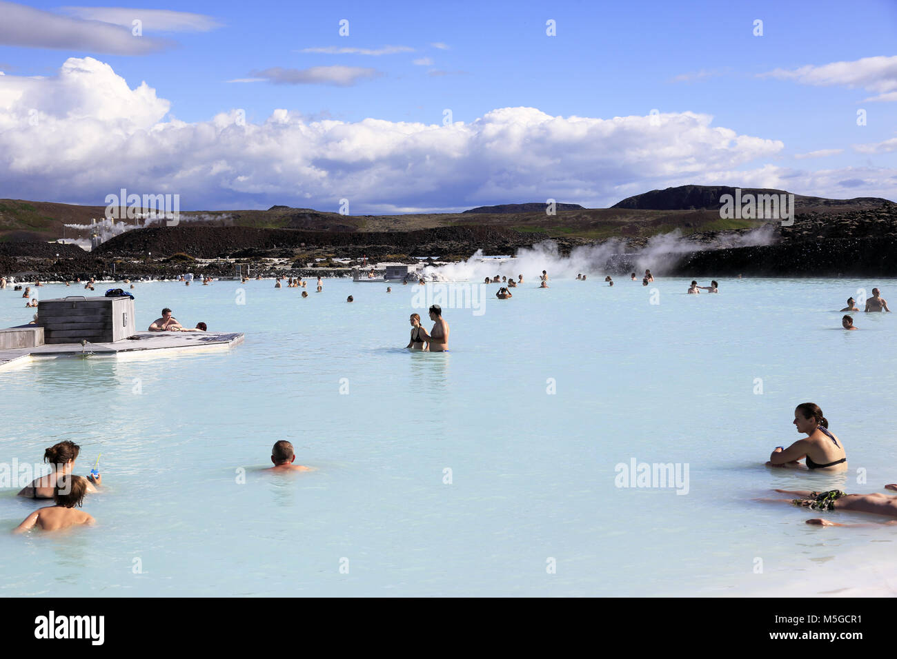 Visitors relax in the geothermal spa of the Blue Lagoon with Svartsengi geothermal power plant in the background.near Reykjavik.Iceland Stock Photo