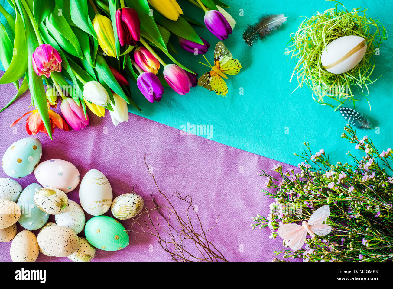Happy Easter shot from above as flatlay with retro easter eggs, butterfly, easter nest and a bunch of tulips in front of colourful background symboliz Stock Photo