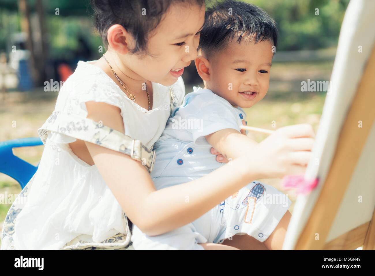 Asian little boy and sister draw together in park. Kids painting and drawing. Children paint with paintbrush color and pencils. Art and crafts for tod Stock Photo