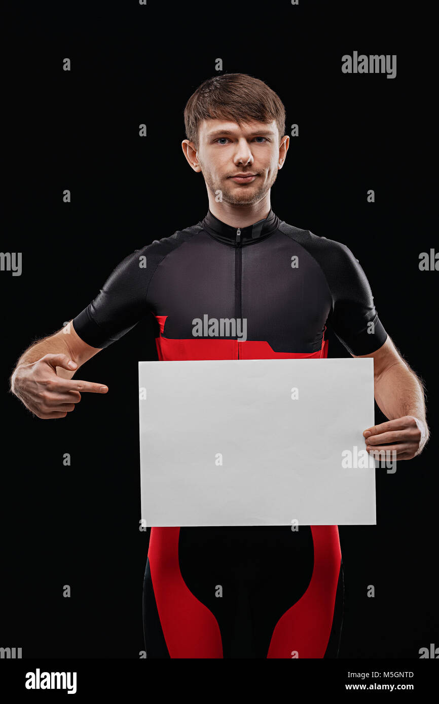 Sport. Cyclist in training clothes on black background holding blank sheet of paper. Your text here. Stock Photo
