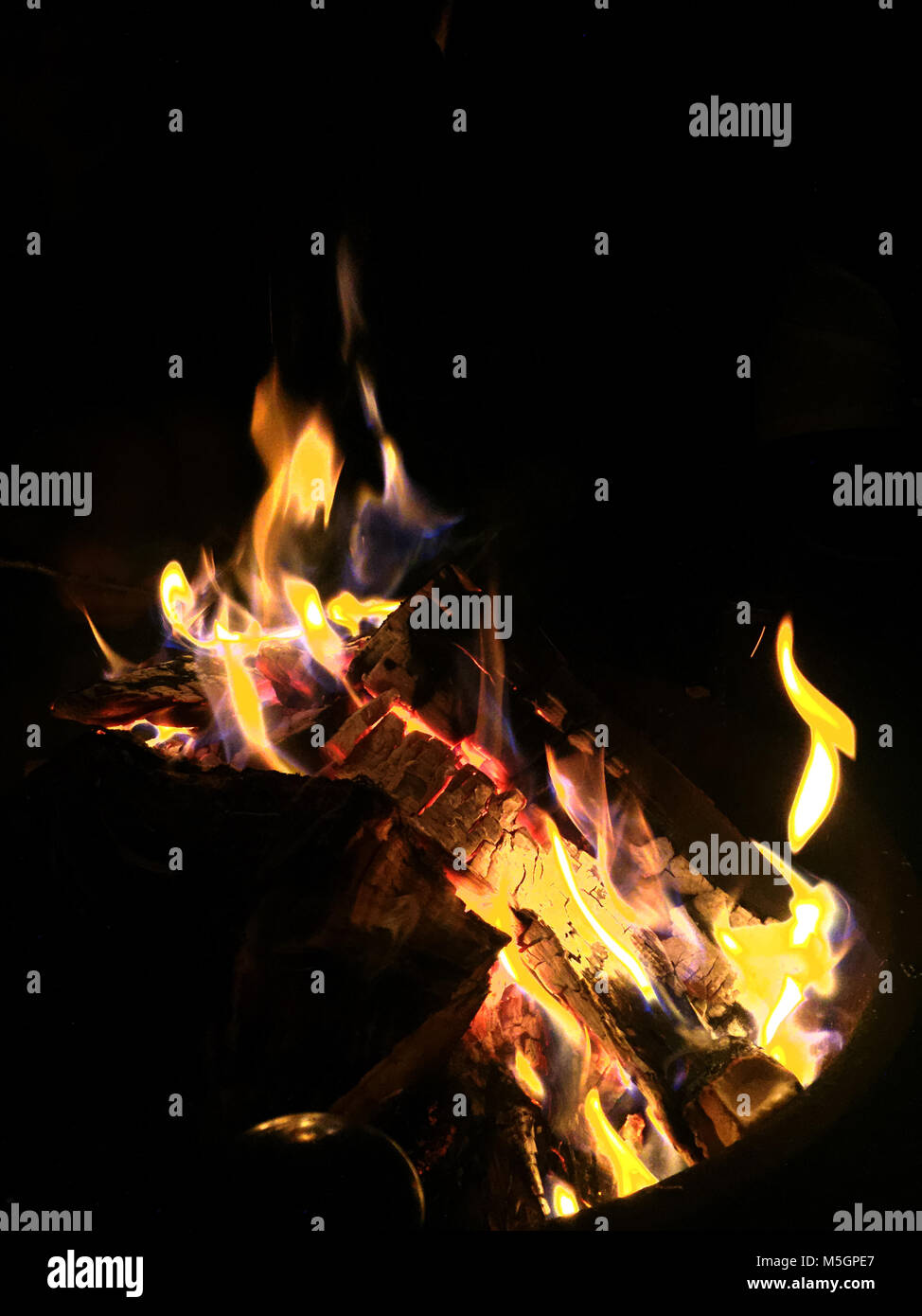 Fire in fire pit, burning wood and embers at night, black background