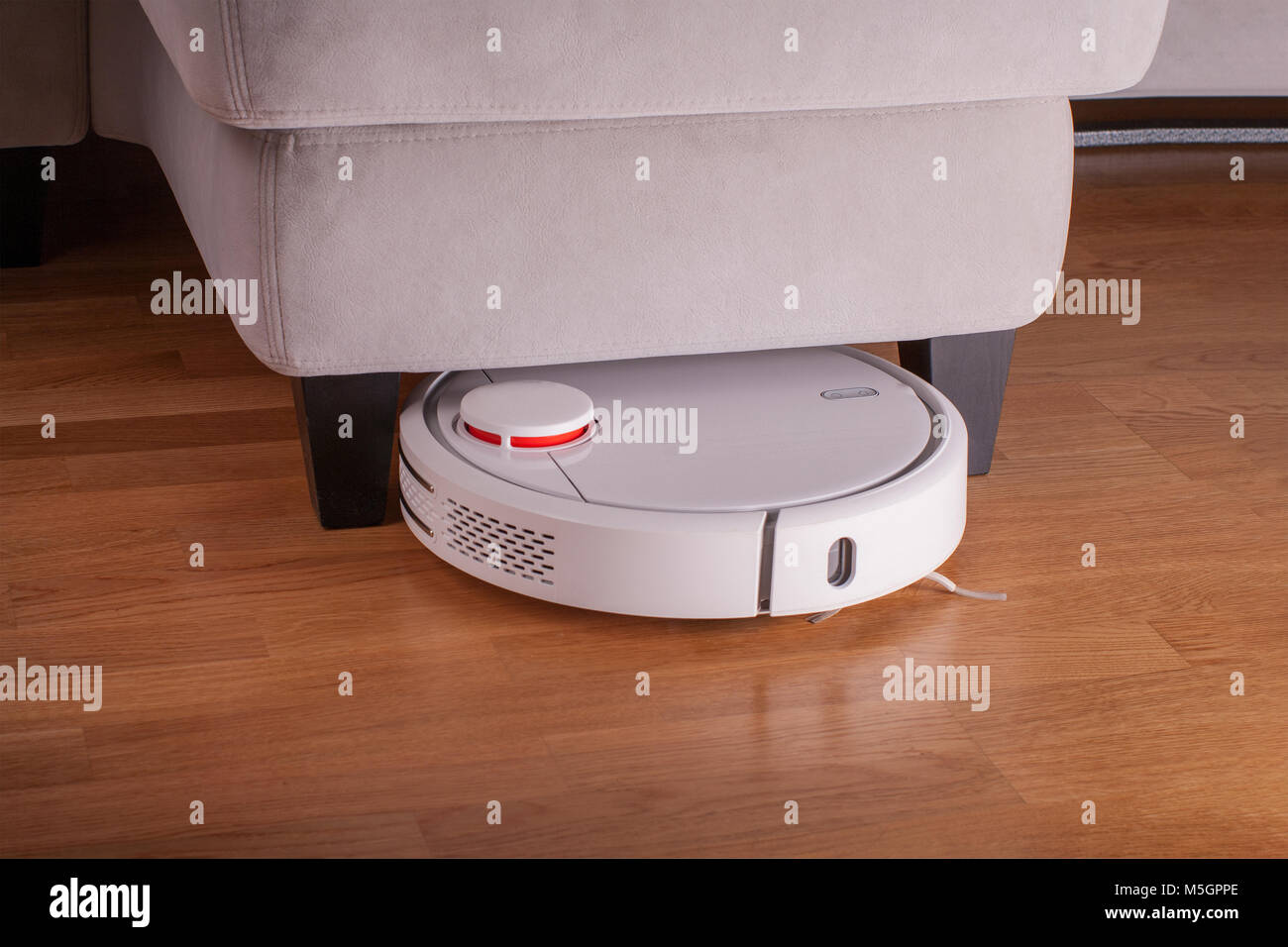 Robot vacuum cleaner runs under sofa in room. Stock Photo