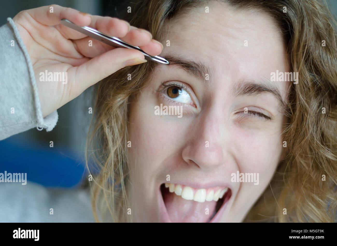 Photograph of a girl plucking her eyebrows with tweezers Stock Photo