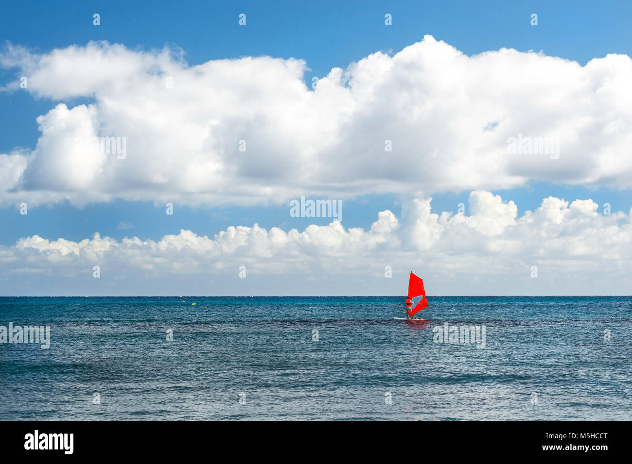 Windsurf with red sail rides on sea. View from sunny Livadi beach in resort village Bali. Rethymno, Crete Greece. Extreme water sports as active recre Stock Photo