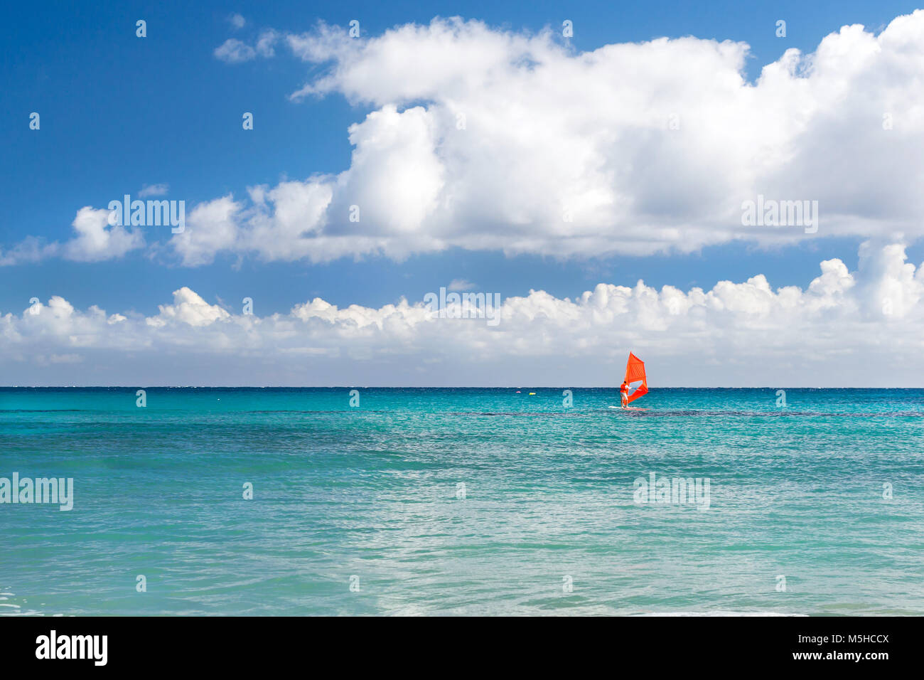 Windsurf with red sail rides on sea. View from sunny Livadi beach in resort village Bali. Rethymno, Crete Greece. Extreme water sports as active recre Stock Photo