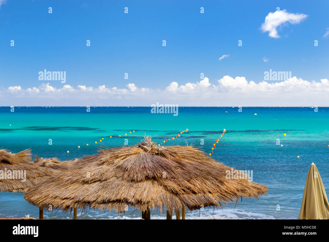 Thatched umbrellas on the beach cafe on the seafront. Livadi beach in sea bay of resort village Bali in may. Bali, Crete, Greece Stock Photo