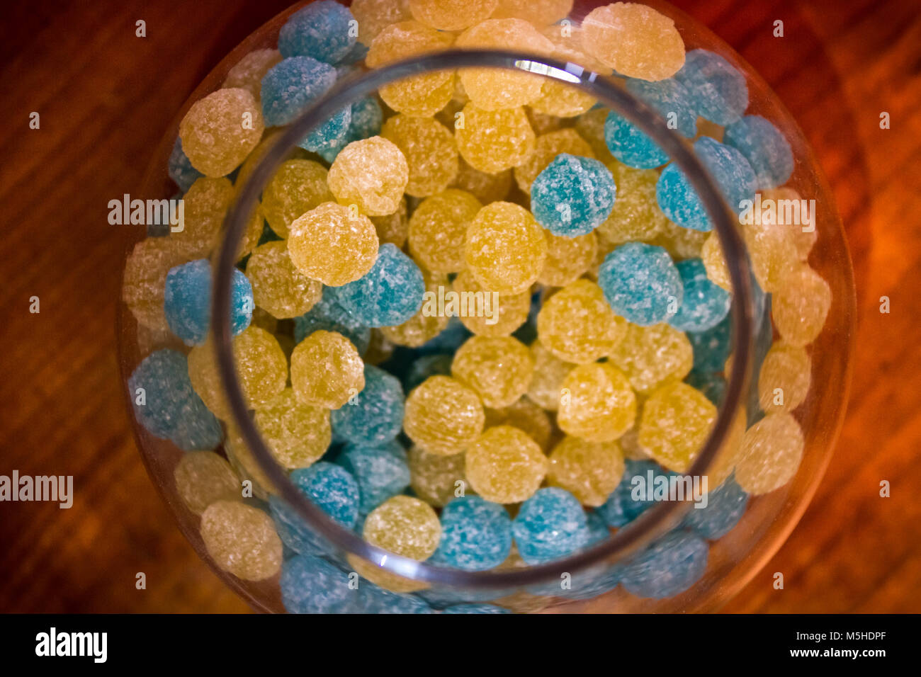 Opened glass jar with round frosty yellow and blue candy on wooden table Stock Photo