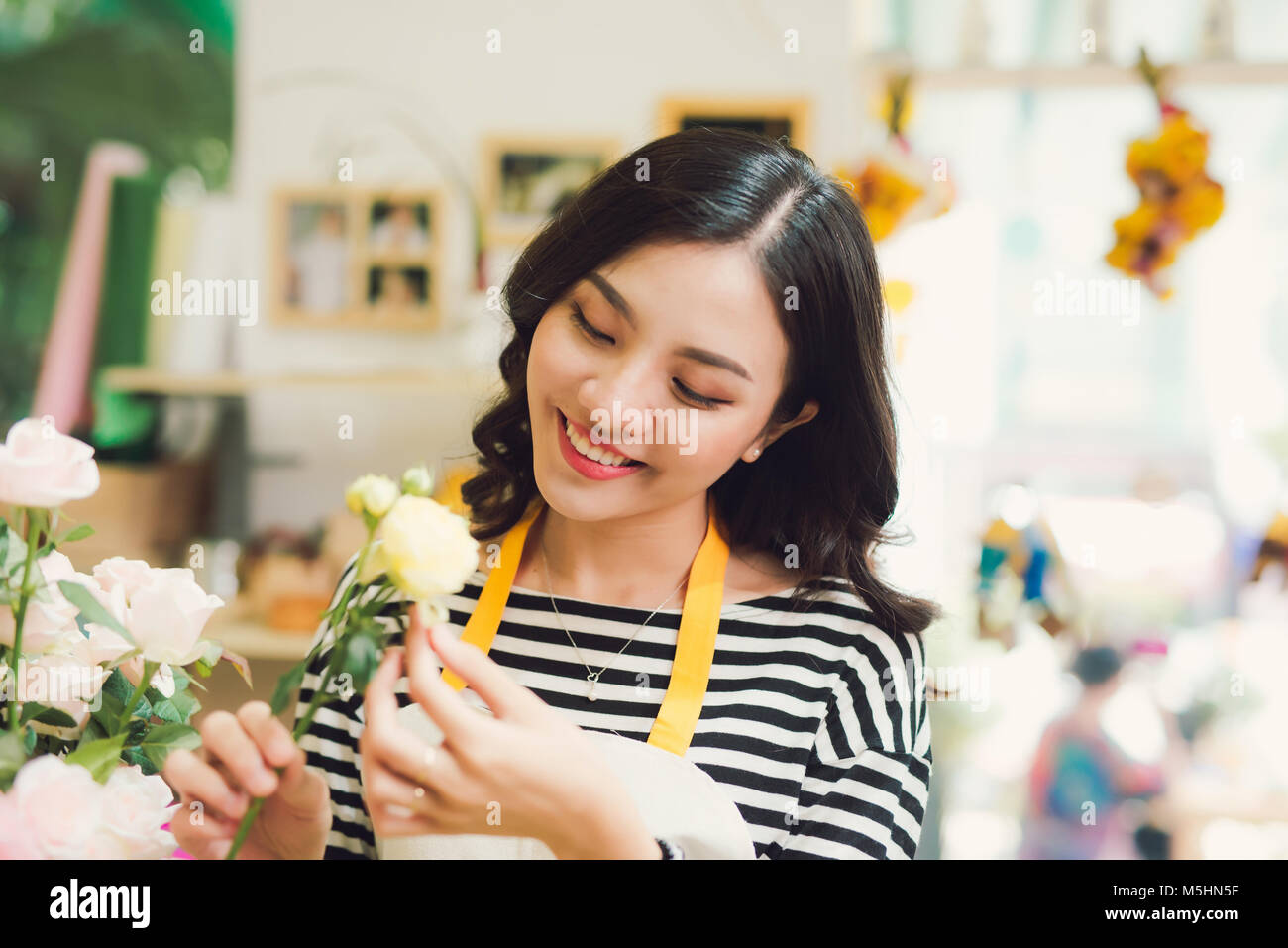 Young beautiful asian girl florist taking care of flowers at workplace ...