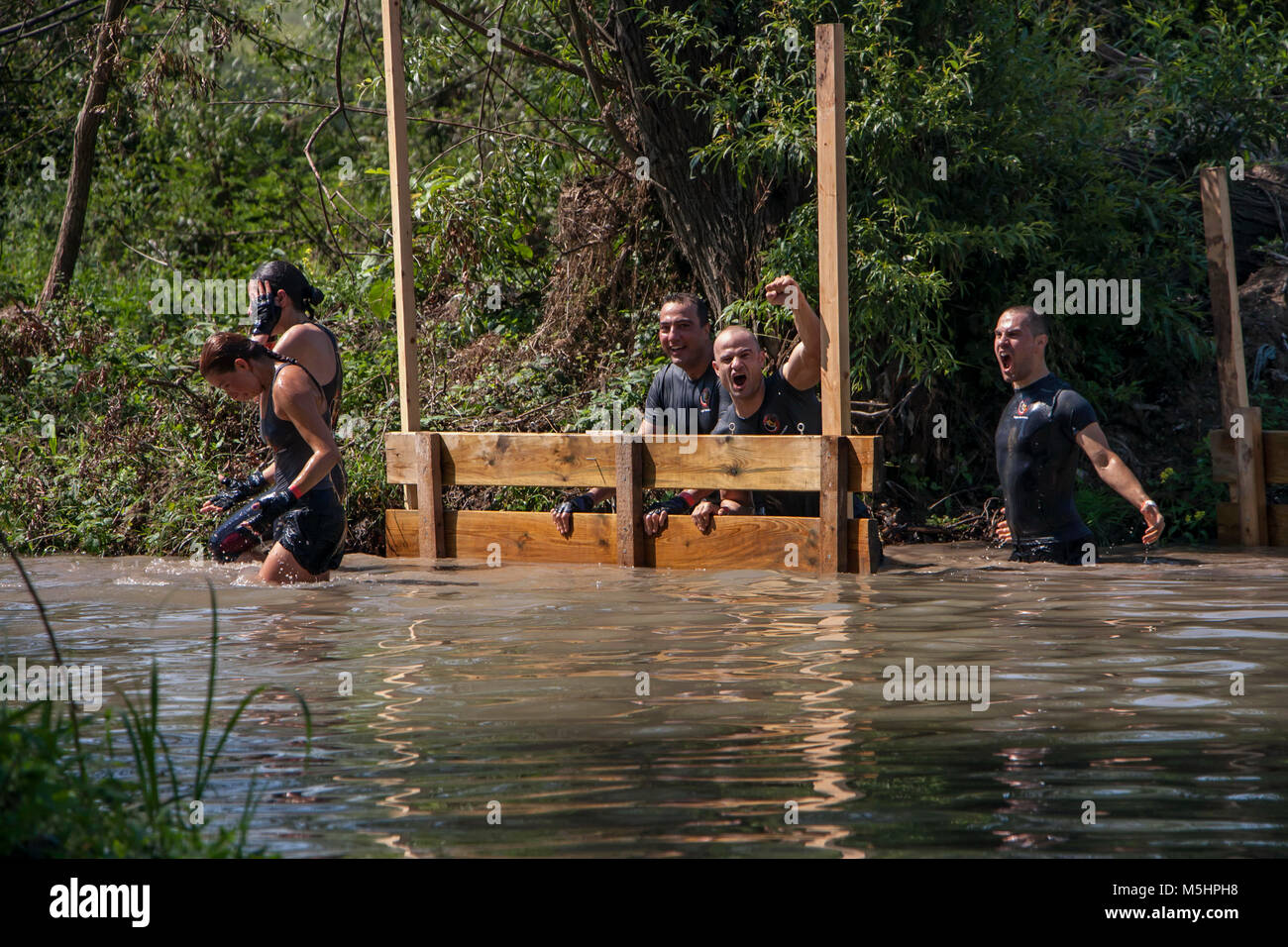A team of three men and two women crossing a river challenge and having fun at the physical strength competition Legion Run held in Sofia, Bulgaria Stock Photo