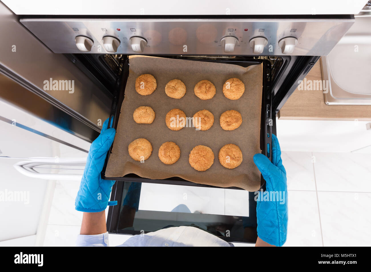 High Angle View Of A Human Hand Taking Out Tray Of Baked Cookies From Oven Stock Photo