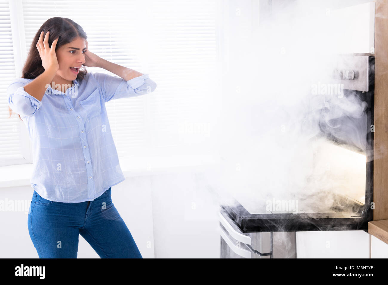 Shocked Young Woman Looking At Smoke Coming From Oven In Kitchen Stock