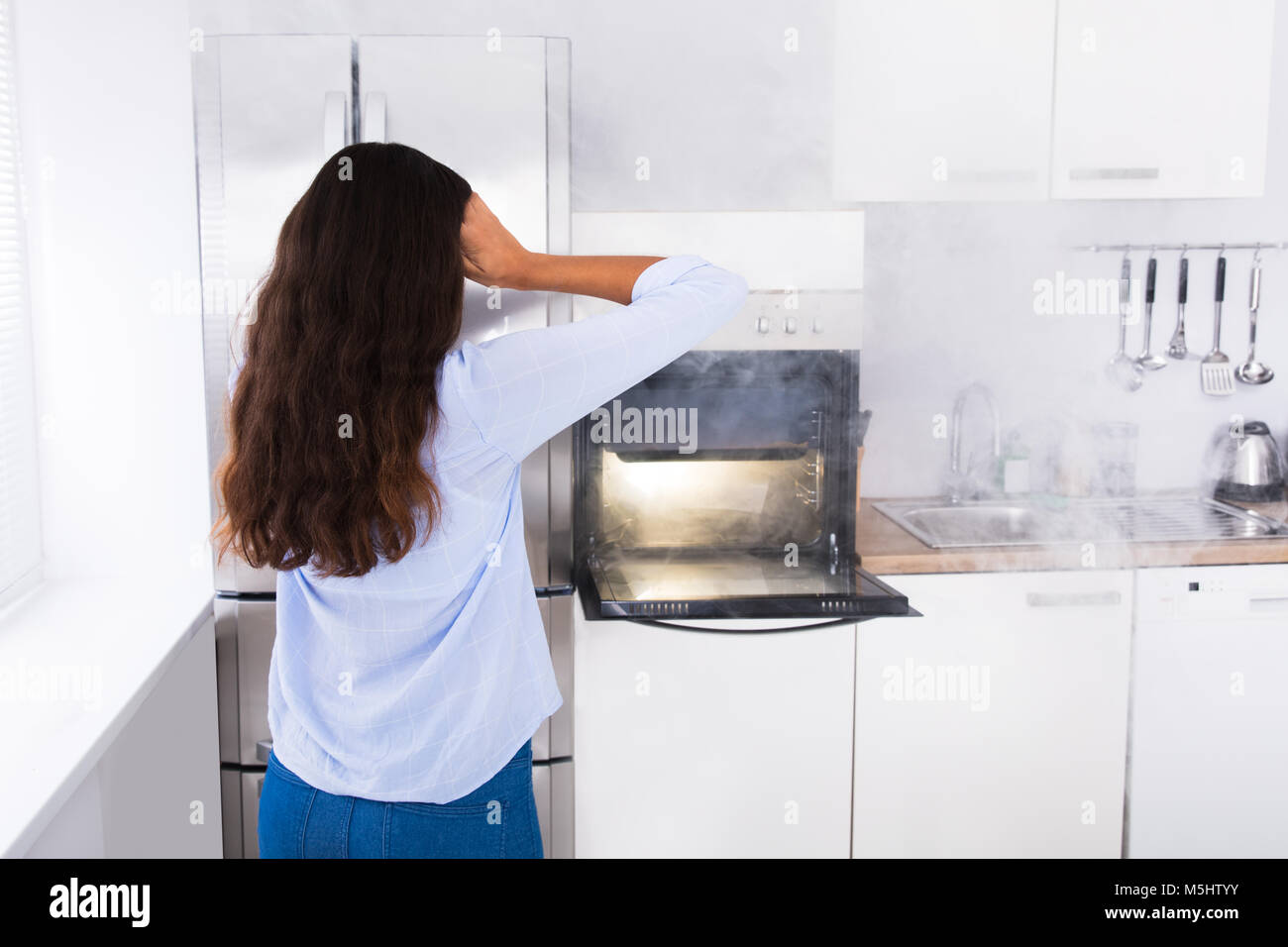 Shocked Young Woman Looking At Smoke Coming From Oven In Kitchen Stock