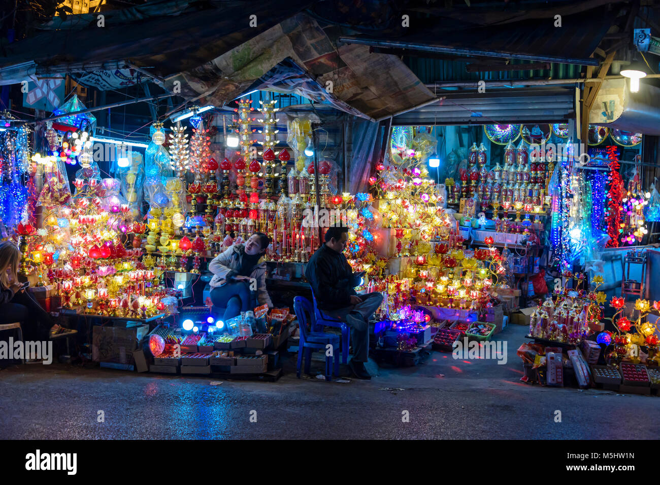 Shopkeepers sit outside their shop on 'Light Street' (Phung Hung) in Hanoi at night. Stock Photo
