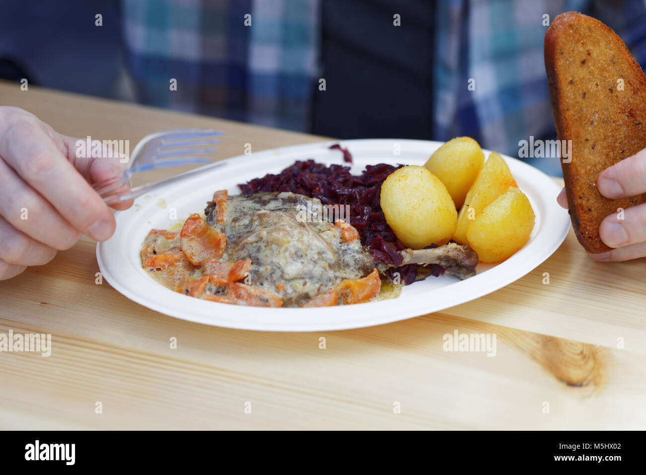 Man eating roasted duck leg with braised red cabbage, boiled potato, and carrot under white sauce in a street food restaurant Stock Photo
