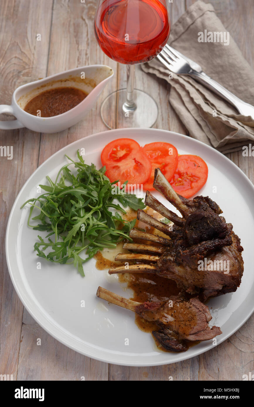 Roasted lamb ribs with rocket salad and tomato on a rustic table Stock ...