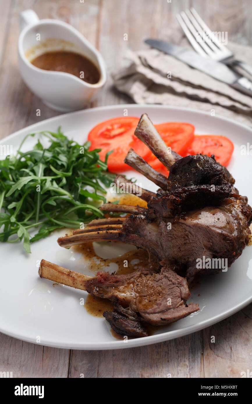Roasted lamb ribs with rocket salad and tomato on a rustic table Stock ...
