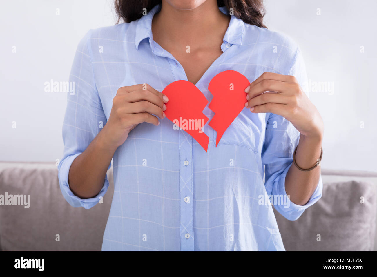 Young Woman Holding Broken Red Valentine Paper Heart At Home Stock Photo