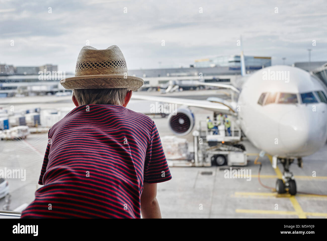 Boy wearing straw hat looking through window to airplane on the apron Stock Photo