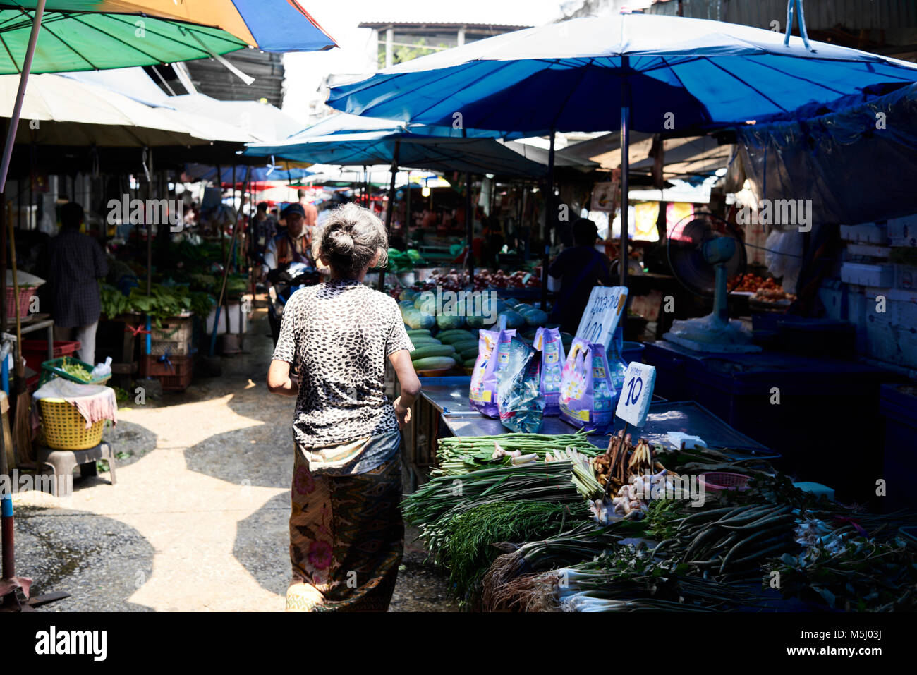 Unrecognizable senior asian woman walking through a colorful street market full of vegetables and fruits. Stock Photo