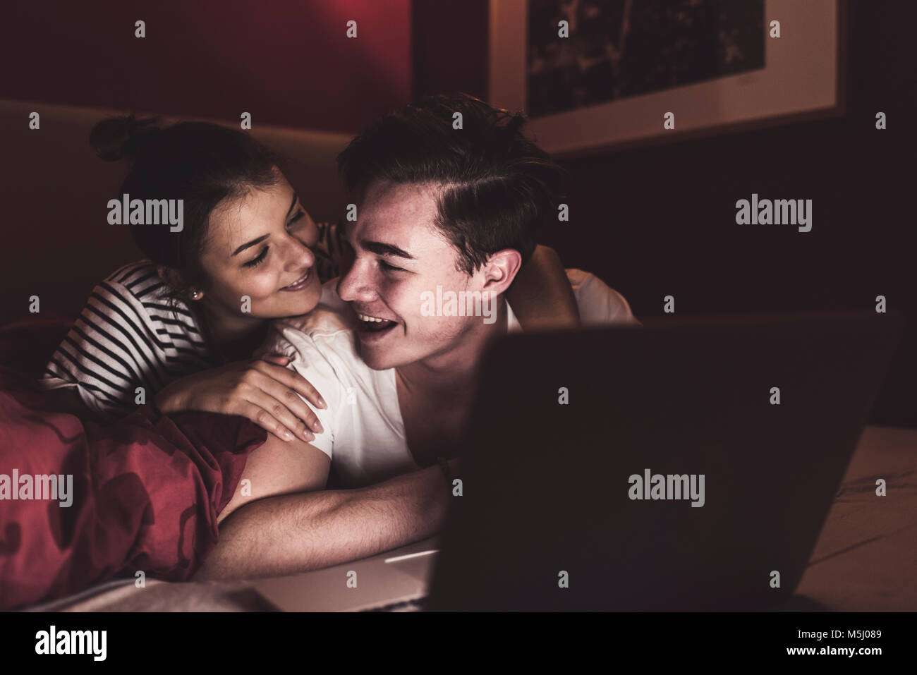 Happy couple lying in bed at home with laptop Stock Photo - Alamy