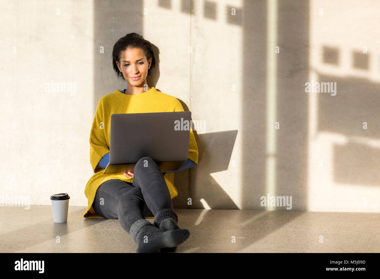 Portrait of smiling young woman sitting on the floor using laptop Stock ...