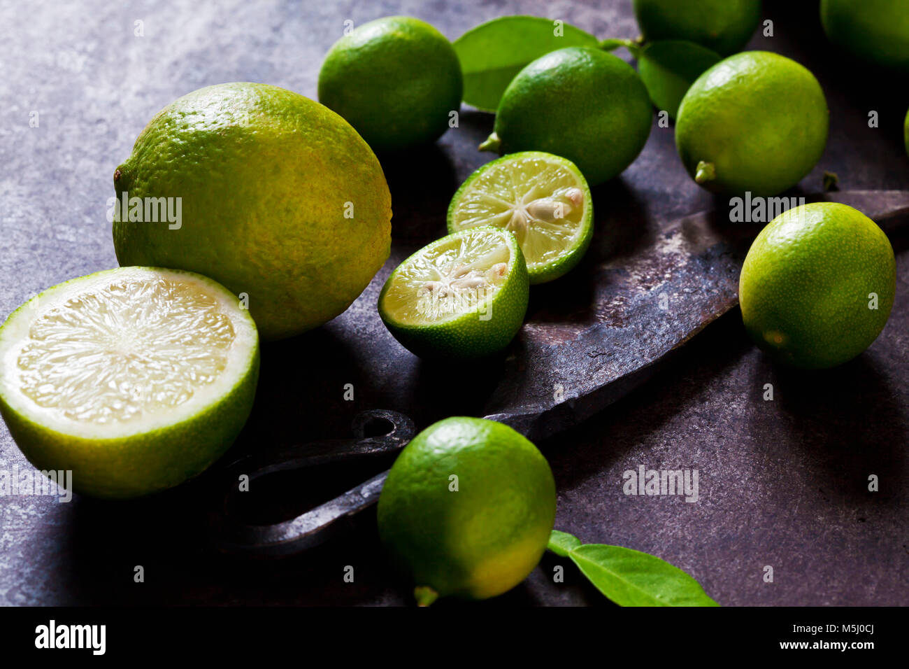 Sliced and whole limequats, limes, leaves and old knife on rusty ground Stock Photo