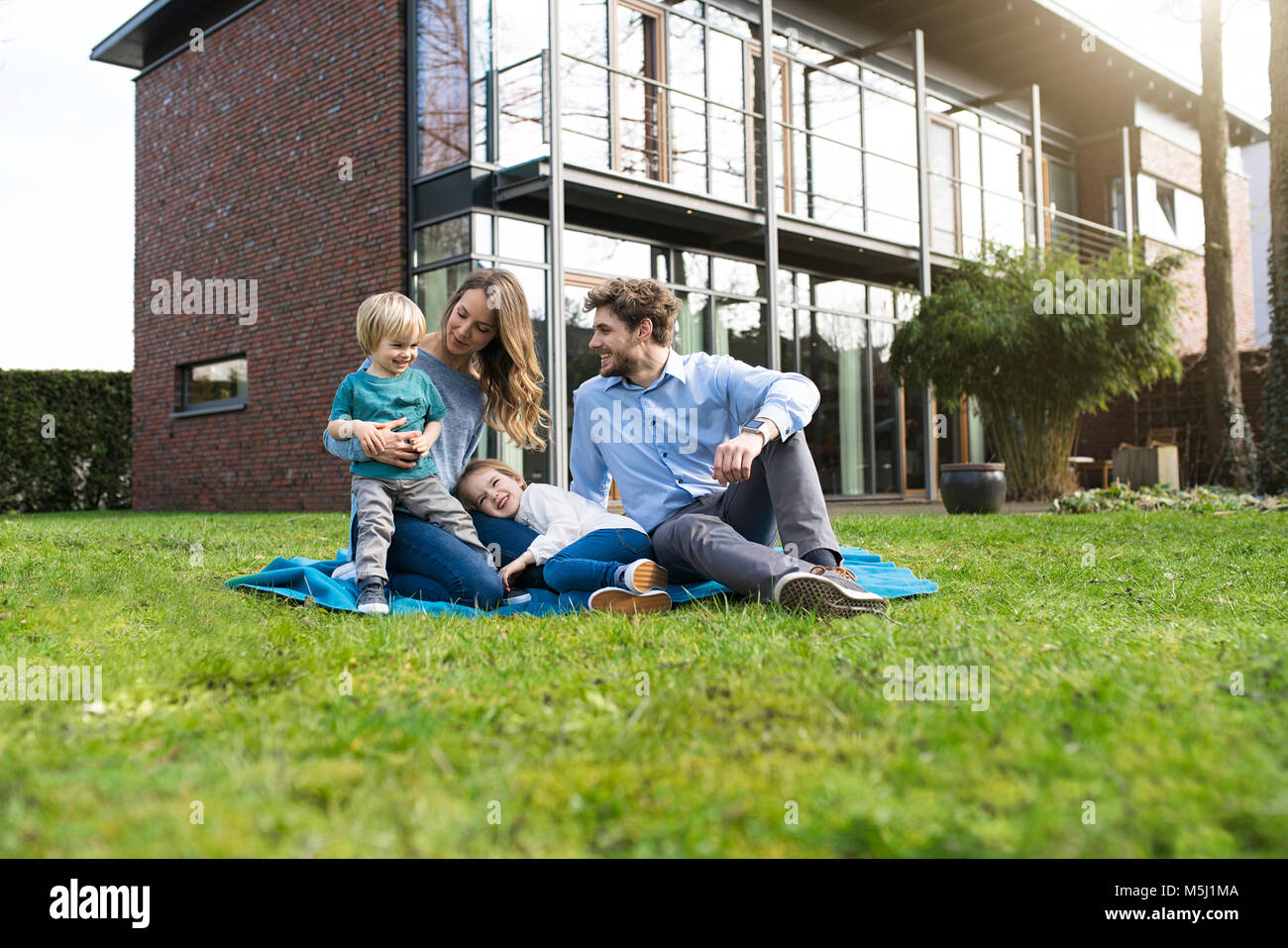 Happy family on blanket in garden in front of their home Stock Photo