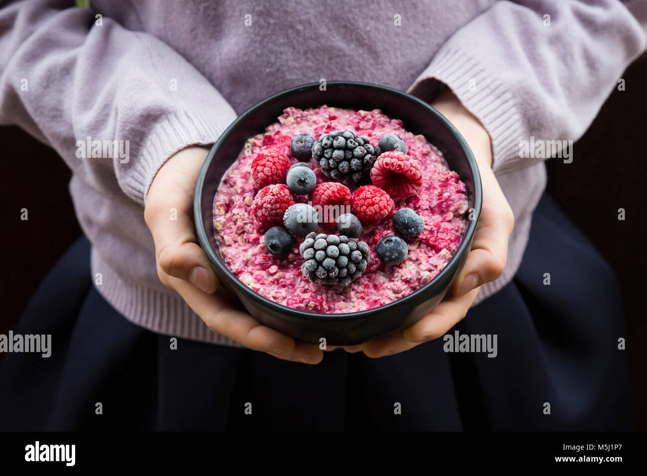 Girl holding bowl with overnight oats mit frozen berries Stock Photo