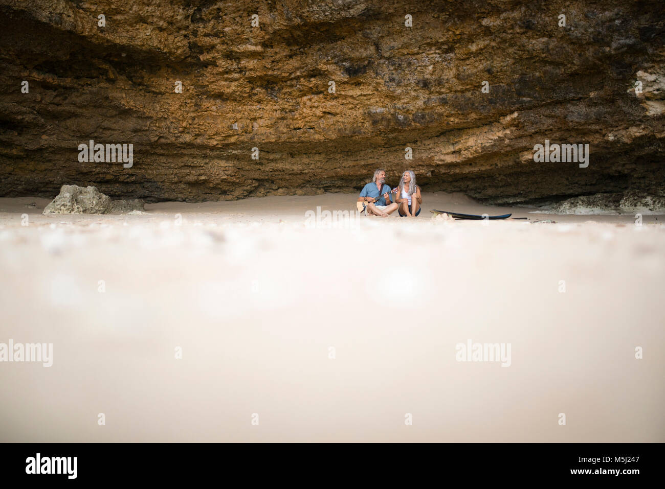 Handsome senior couple sitting on the beach, man playing guitar Stock Photo