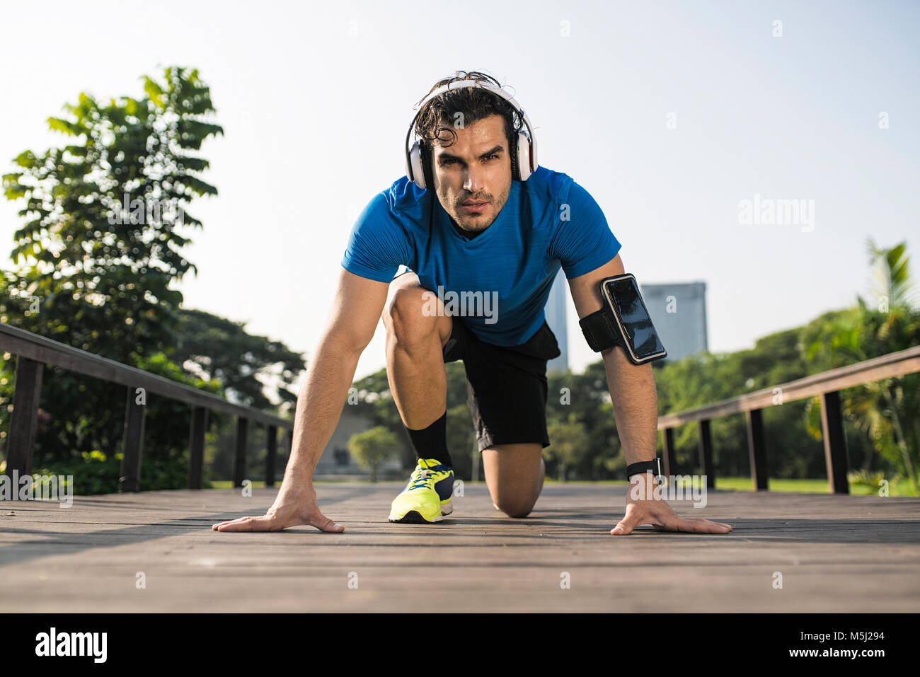 Runner training start position on street in urban park, wearing headphones Stock Photo