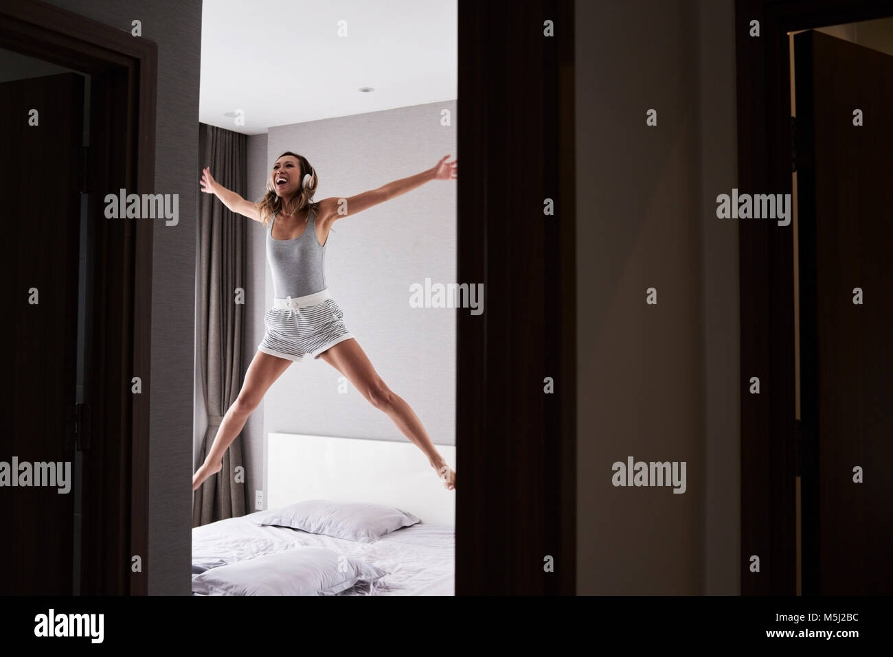 Happy asian woman jumping released in bed with headphones. Give me music. Stock Photo