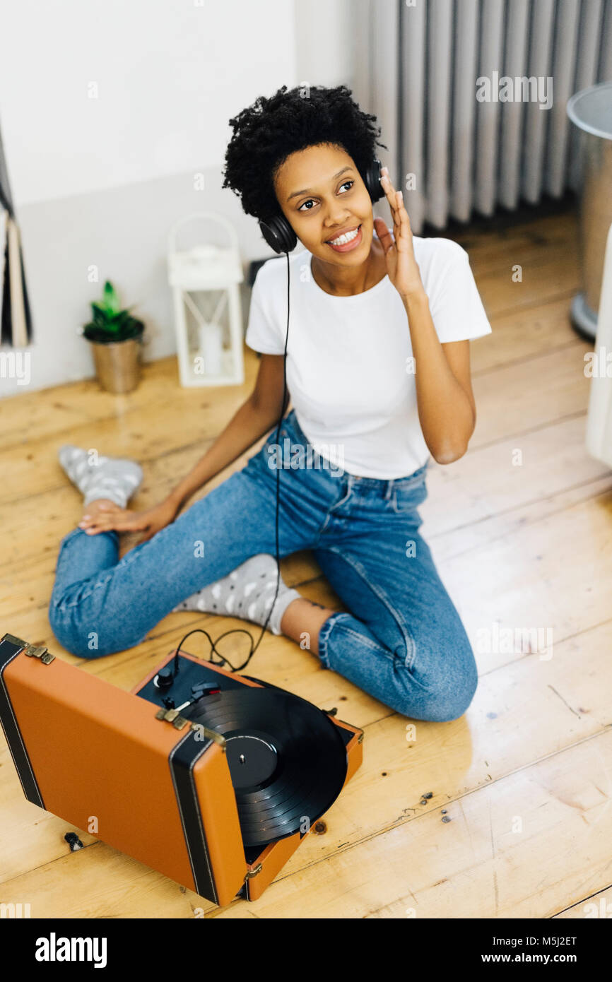 Young woman sitting on grounf listening music from record player, using headphones Stock Photo