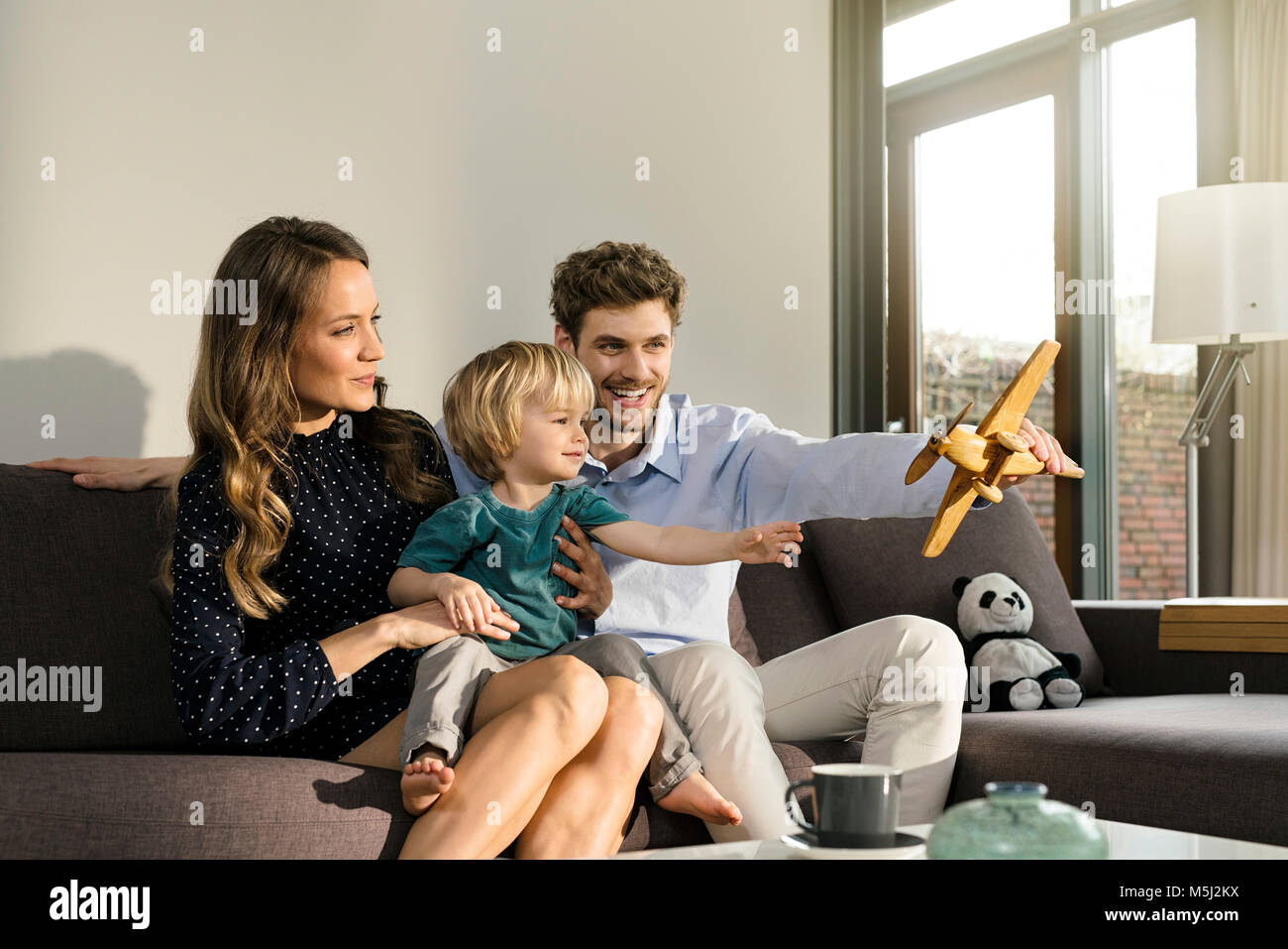 Happy parents and son playing with wooden toy plane on sofa at home Stock Photo