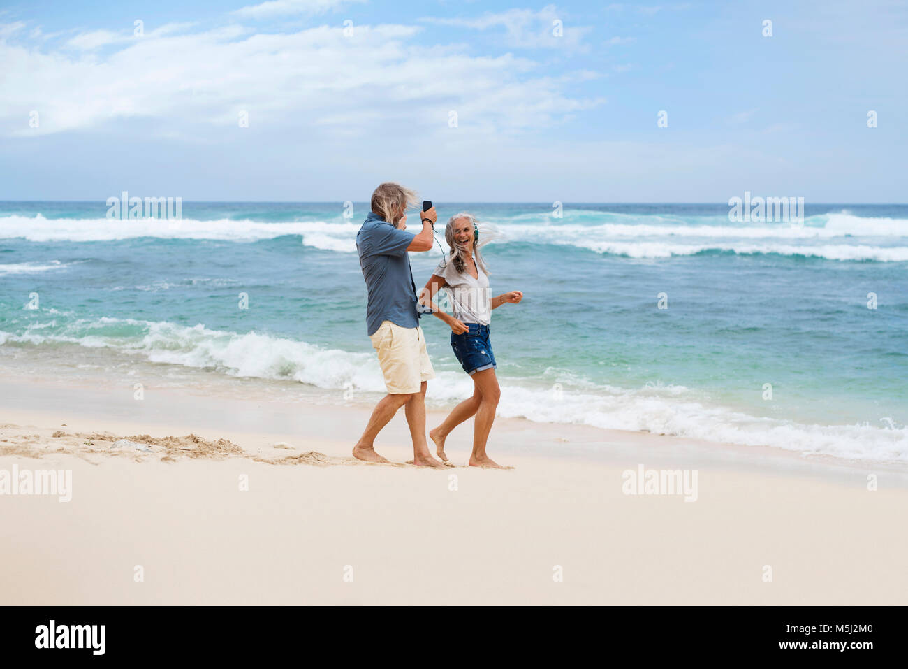 Handsome senior couple with headphones dancing on the beach Stock Photo