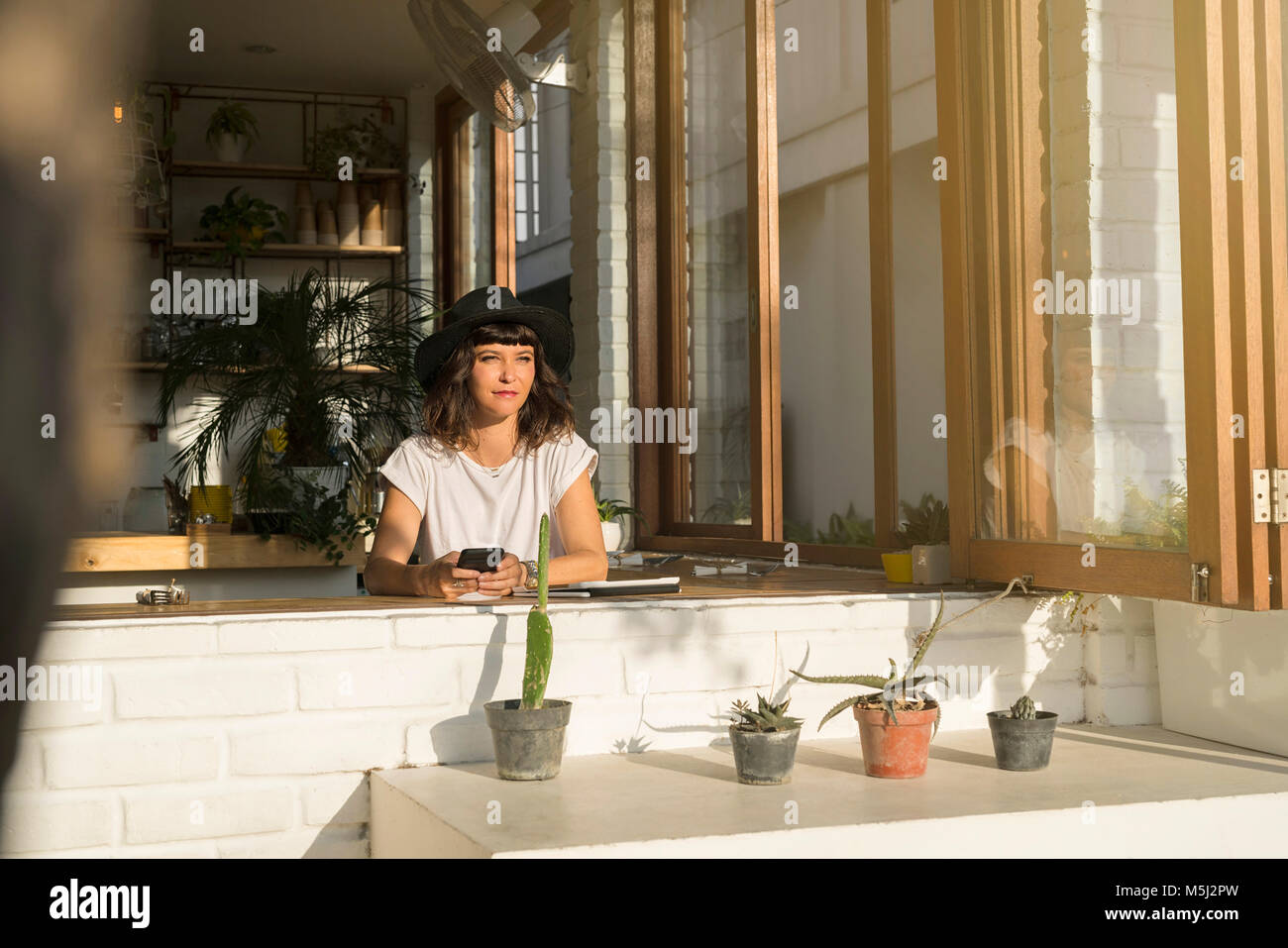 Woman with hat and smartphone sitting in a cafe Stock Photo