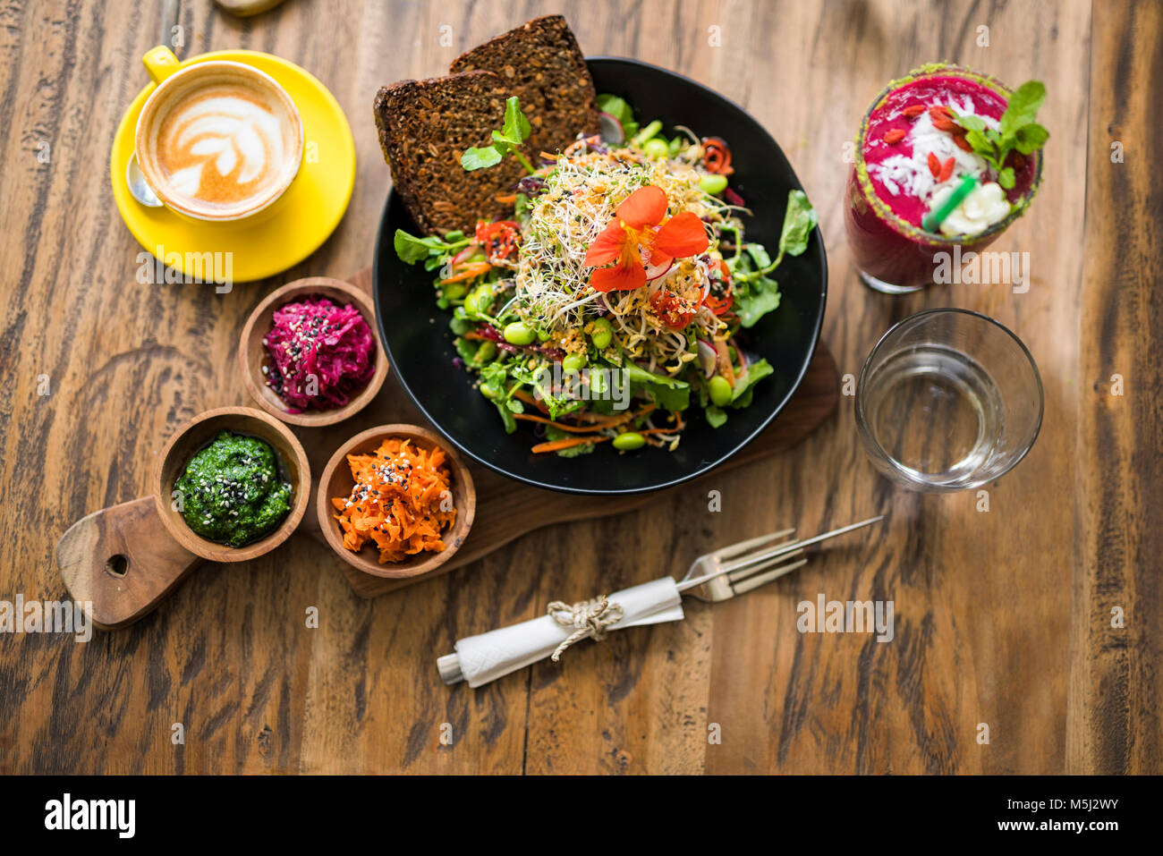 Decorated colorful salad on wooden plate with coffee, water and smoothie on the side Stock Photo
