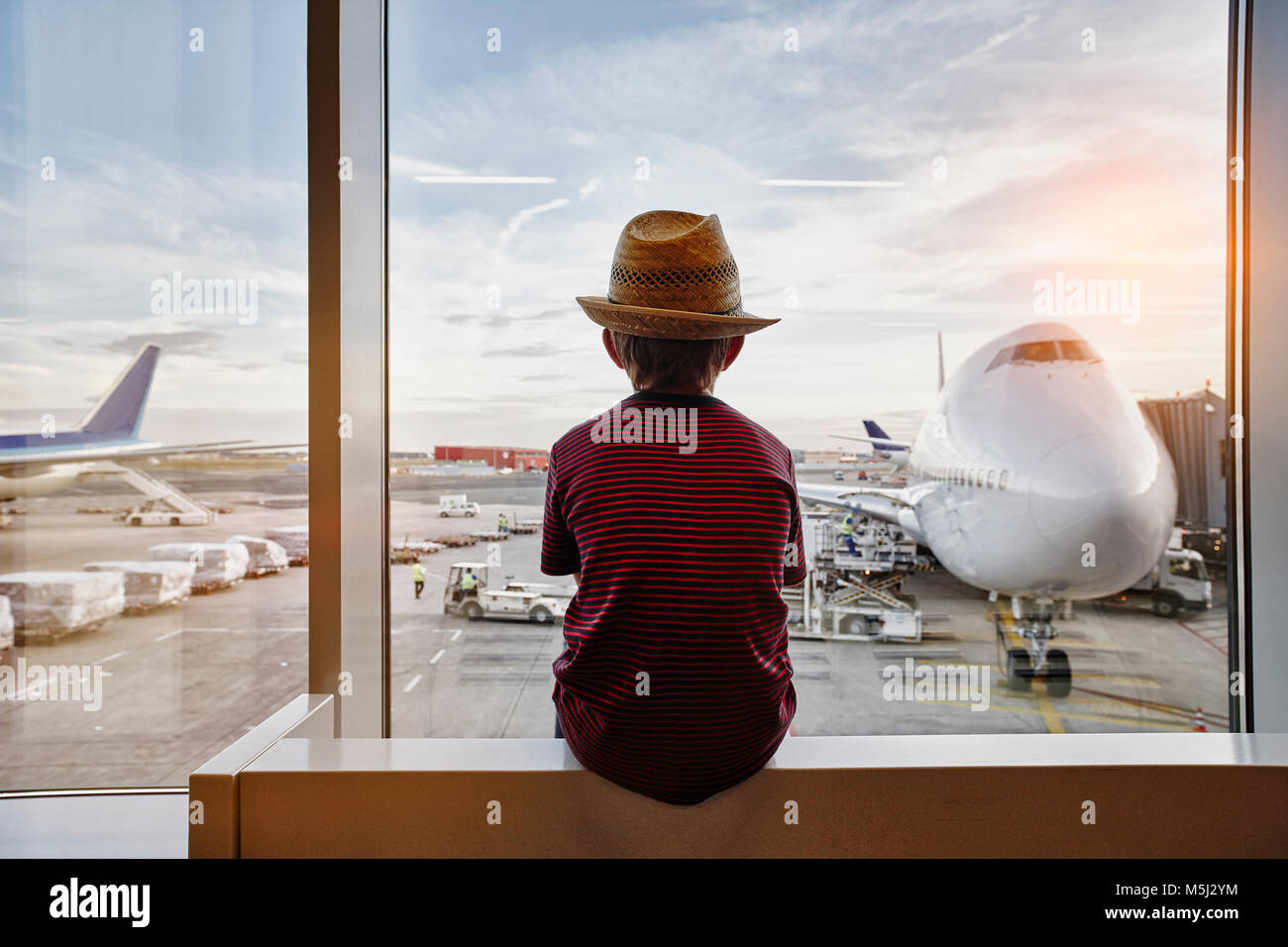 Boy wearing straw hat looking through window to airplane on the apron Stock Photo