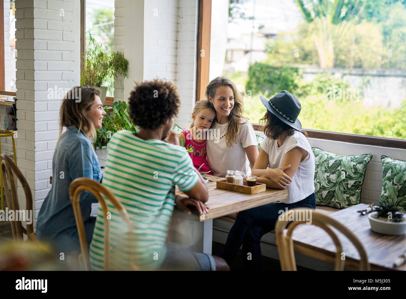 Happy friends with child socializing in cozy cafe Stock Photo