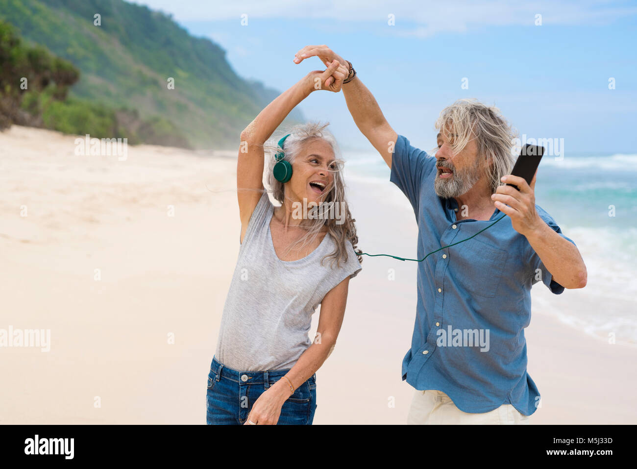 Handsome senior couple with headphones dancing on the beach Stock Photo