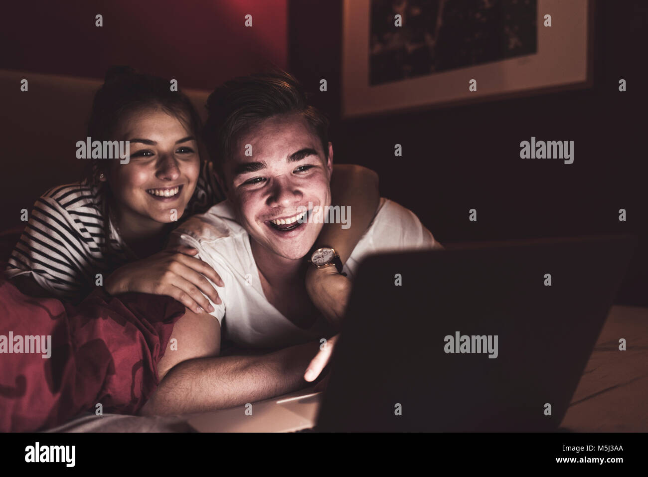 Happy couple lying in bed at home looking at laptop Stock Photo - Alamy