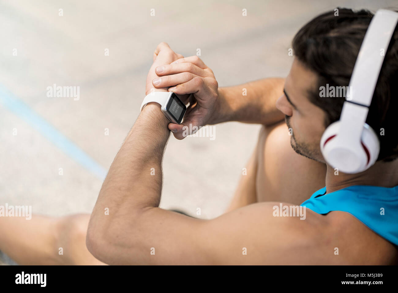 Athlete with earphones sitting on the ground, checking his smartwatch Stock Photo
