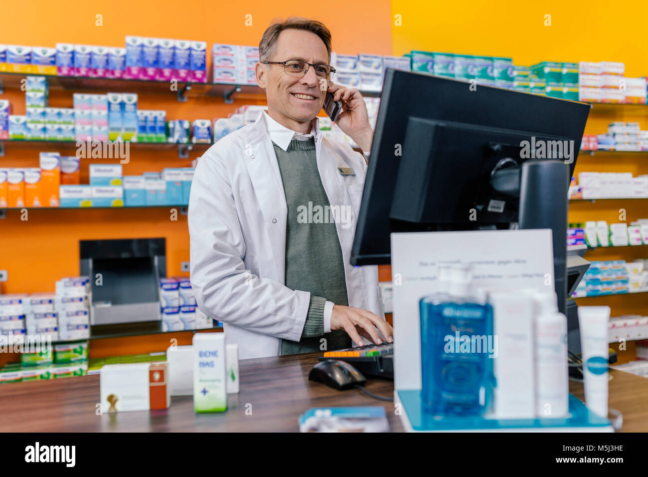 Smiling pharmacist talking on phone at counter in pharmacy Stock Photo