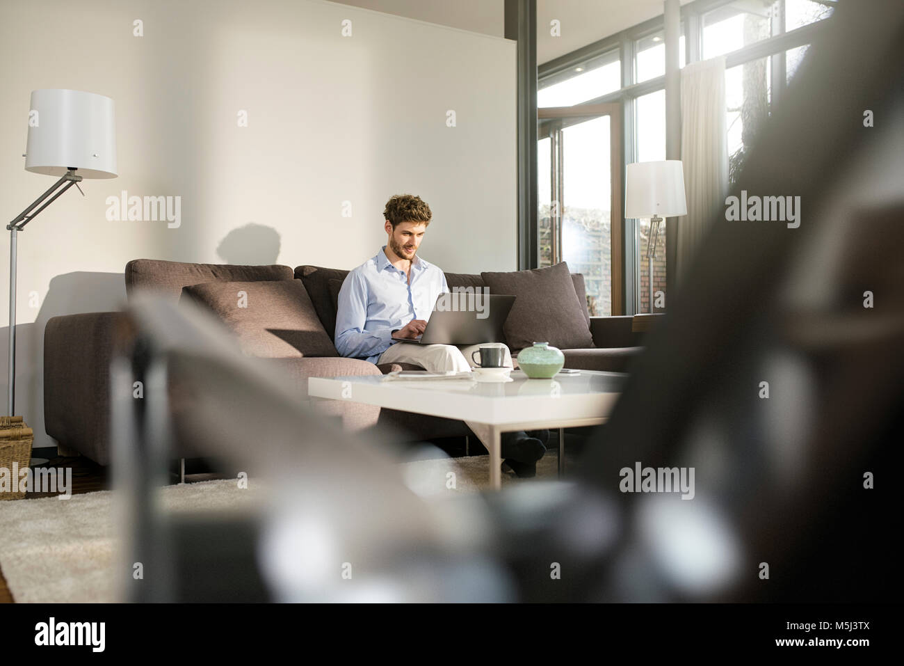 Man sitting on couch at home using laptop Stock Photo